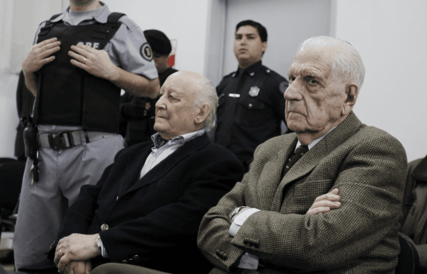 O ex-presidente da junta militar argentina, Reynaldo Bignone (à direita), e o ex-general Santiago Riveros (ao centro), durante o julgamento por crimes contra a humanidade em 2012. (Créditos: Leo la Valle/via EPA)