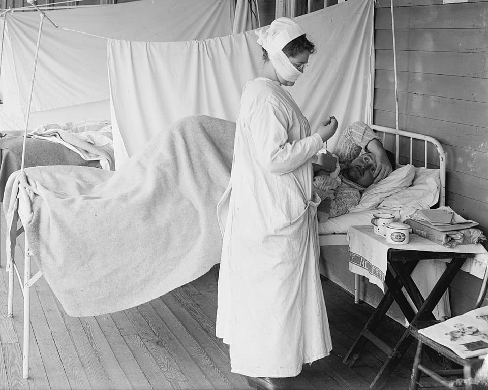 Uma enfermeira usa máscara de tecido enquanto trata um paciente com gripe em Washington, DC, por volta de 1919. (Reprodução: Wikipedia)