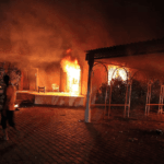 Um veículo e os edifícios circundantes ardem em chamas após terem sido incendiados dentro do complexo do consulado dos EUA em Benghazi, no final do dia 11 de setembro de 2012. (Créditos: AFP/via Getty Images, FILE)