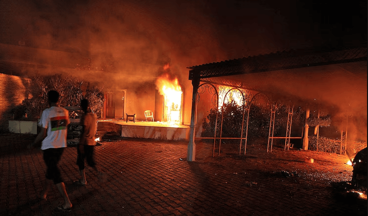 Um veículo e os edifícios circundantes ardem em chamas após terem sido incendiados dentro do complexo do consulado dos EUA em Benghazi, no final do dia 11 de setembro de 2012. (Créditos: AFP/via Getty Images, FILE)