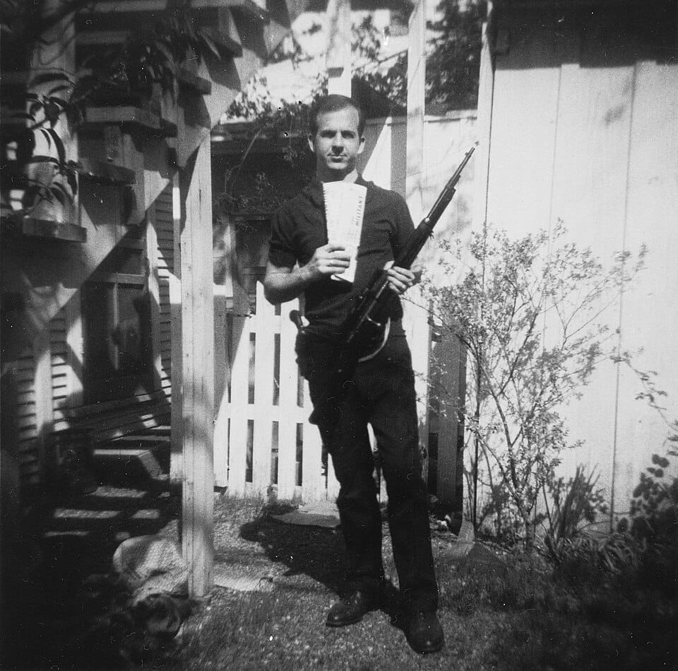 Lee Harvey Oswald segurando um rifle e jornais comunistas em uma foto sem data divulgada pelo Departamento de Polícia de Dallas. (Reprodução: Wikipedia)